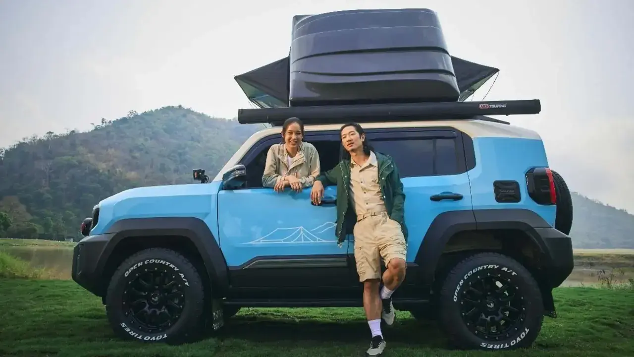 Coppia sorridente accanto a un toyota land cruiser mini blu, pronto per l'avventura con tettoia e box sul tetto.