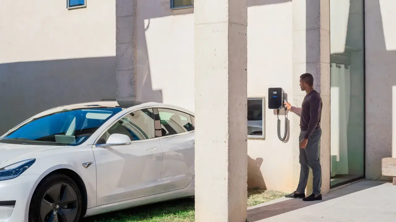 Uomo accanto a un'auto elettrica bianca, che interagisce con una wallbox V2C. Un bonus per la ricarica intelligente.