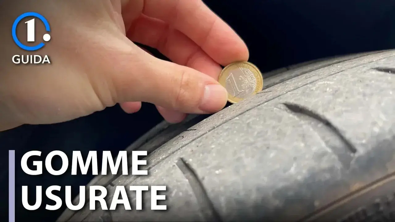 Una mano inserisce una moneta da 1 euro in un solco di uno pneumatico per mostrare come vedere se le gomme sono consumate.