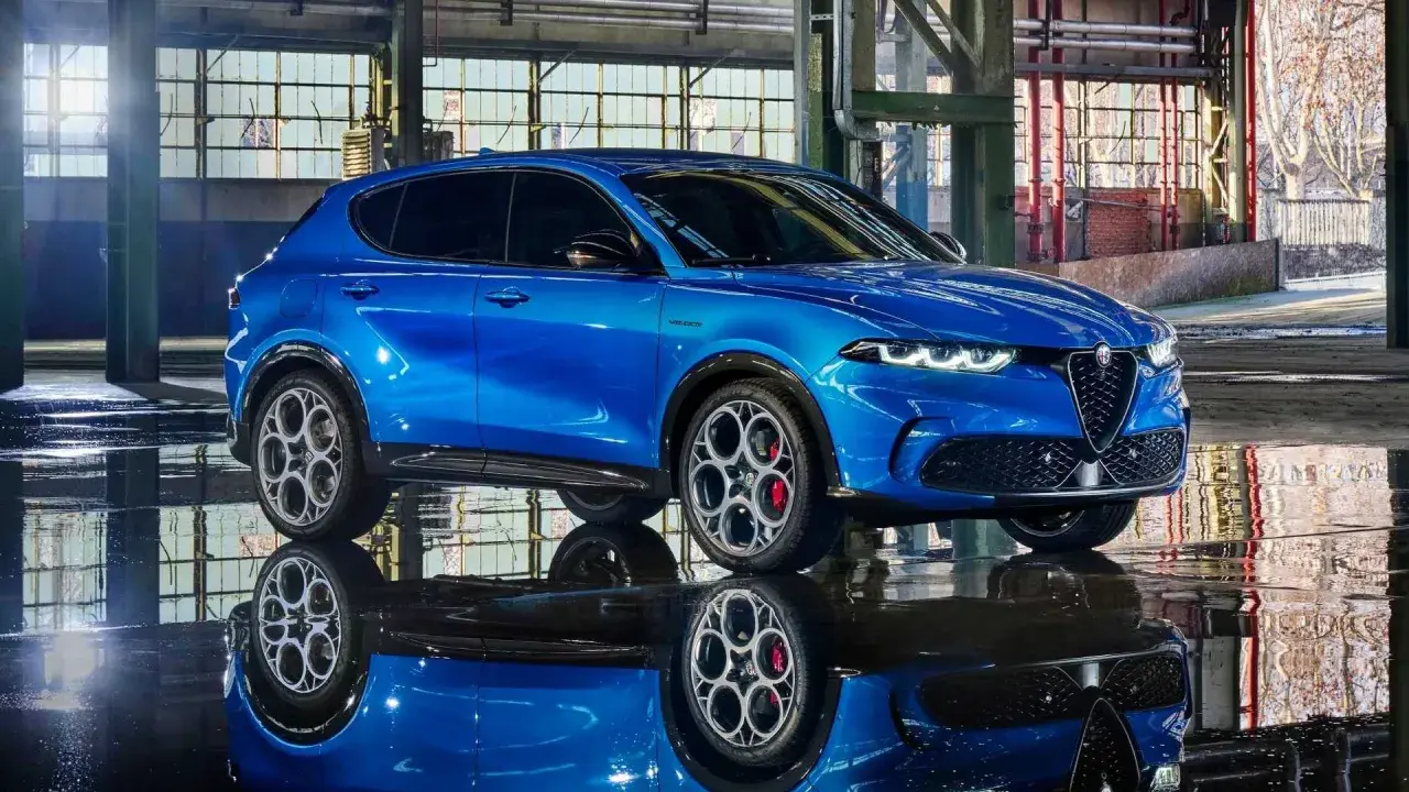 Alfa Romeo Tonale blu, un esempio di stellantis auto elettriche, riflette sul pavimento bagnato di un capannone industriale.