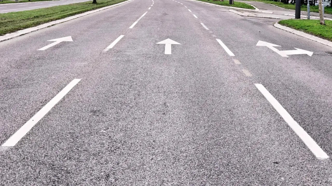 Strada con frecce bianche che indicano le corsie di canalizzazione.