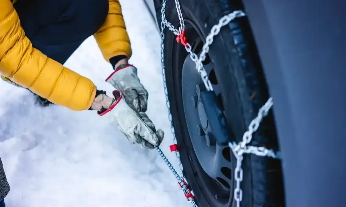 Mani guantate montano le catene da neve su una gomma 4 stagioni. Se ho le gomme 4 stagioni devo avere le catene per la sicurezza invernale.