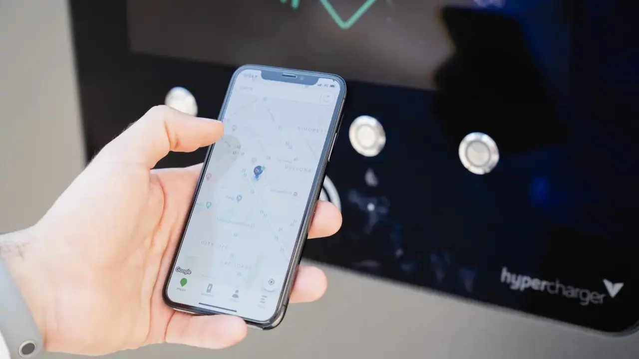 Mano che usa smartphone con mappa per trovare stazione di ricarica. L'app mostra la posizione e le opzioni per monitorare la carica.