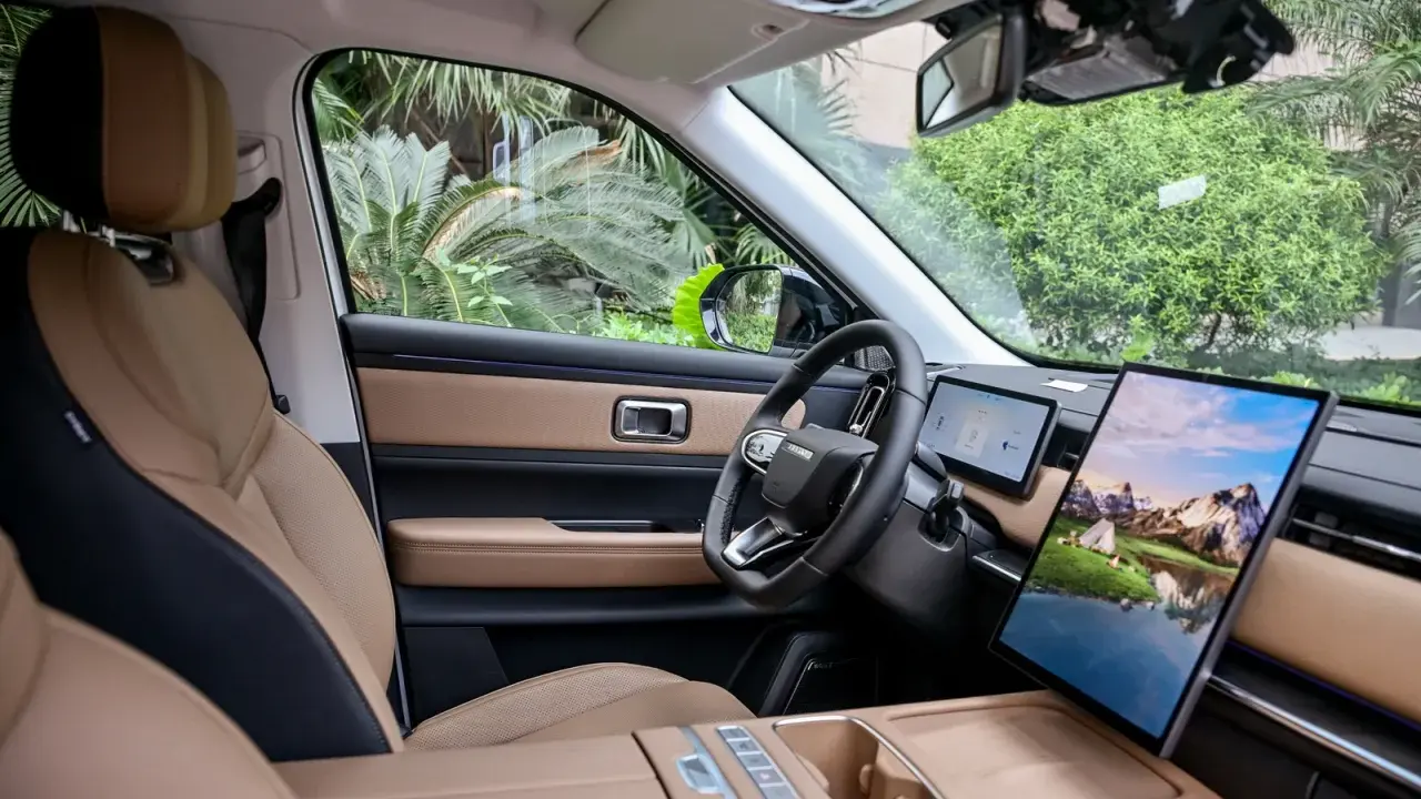 Interni del Jaecoo 7: sedili in pelle beige e nera, volante moderno e un grande schermo centrale con paesaggio montano.