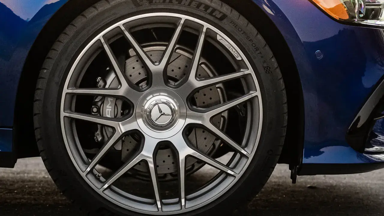 Ruota di un'auto blu con cerchi AMG e freni a disco forati. Il pneumatico Michelin mostra un leggero segno di usura.