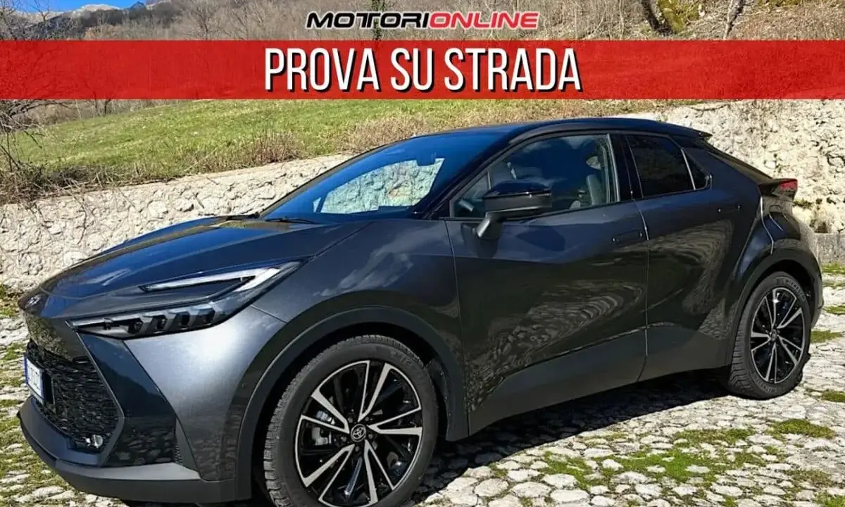 Toyota C-HR grigia parcheggiata su un selciato, con la scritta "PROVA SU STRADA". La sua linea moderna suscita un senso di delusione per chi si aspettava di più.