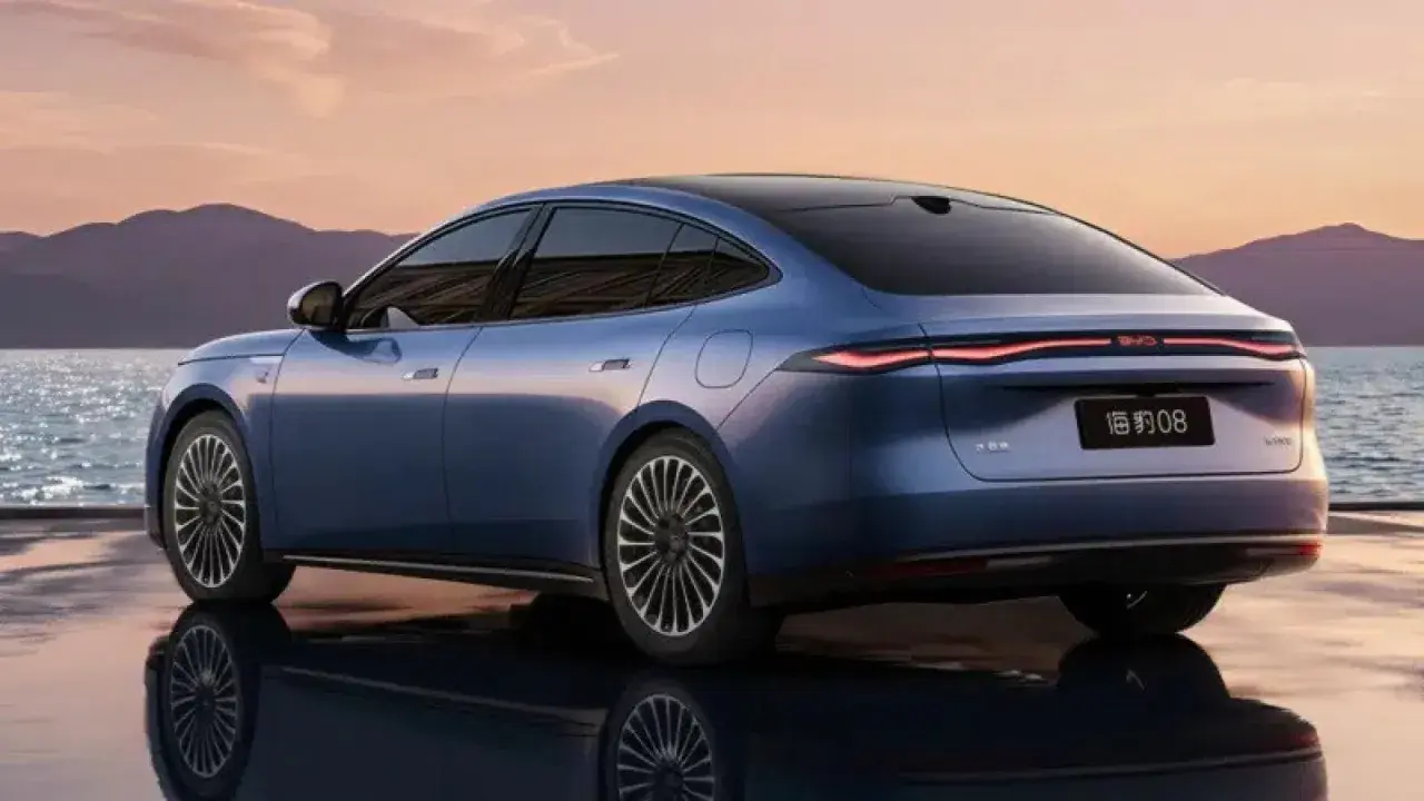 BYD Seal 08, berlina blu elettrica, riflette sull'acqua al tramonto, con montagne sullo sfondo.