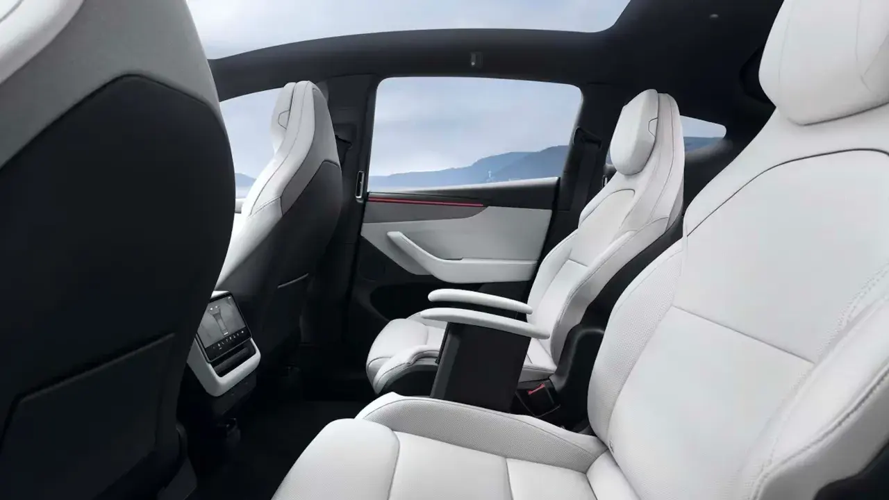 Interni bianchi e neri del Tesla Model Y, con sedili in pelle, tetto panoramico e vista sulle montagne.
