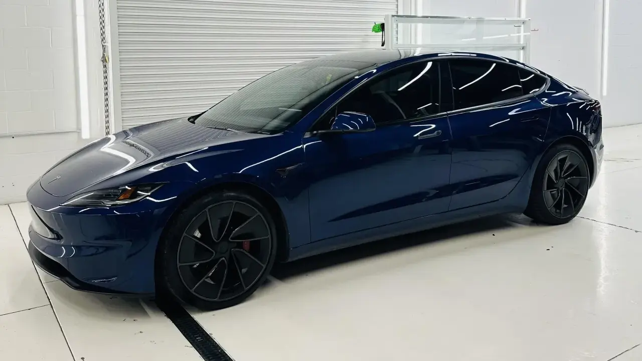 Una splendida Tesla piccola, blu scuro, con cerchi neri lucidi, parcheggiata in un garage pulito e illuminato.