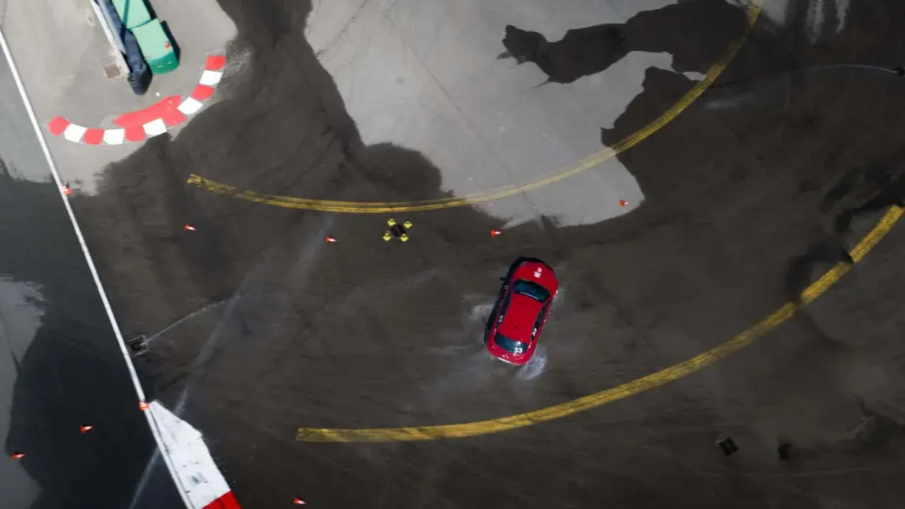 Auto rossa in derapata su asfalto bagnato, con coni arancioni e segnali di pista. I pneumatici Kumho mostrano i loro limiti in condizioni difficili.