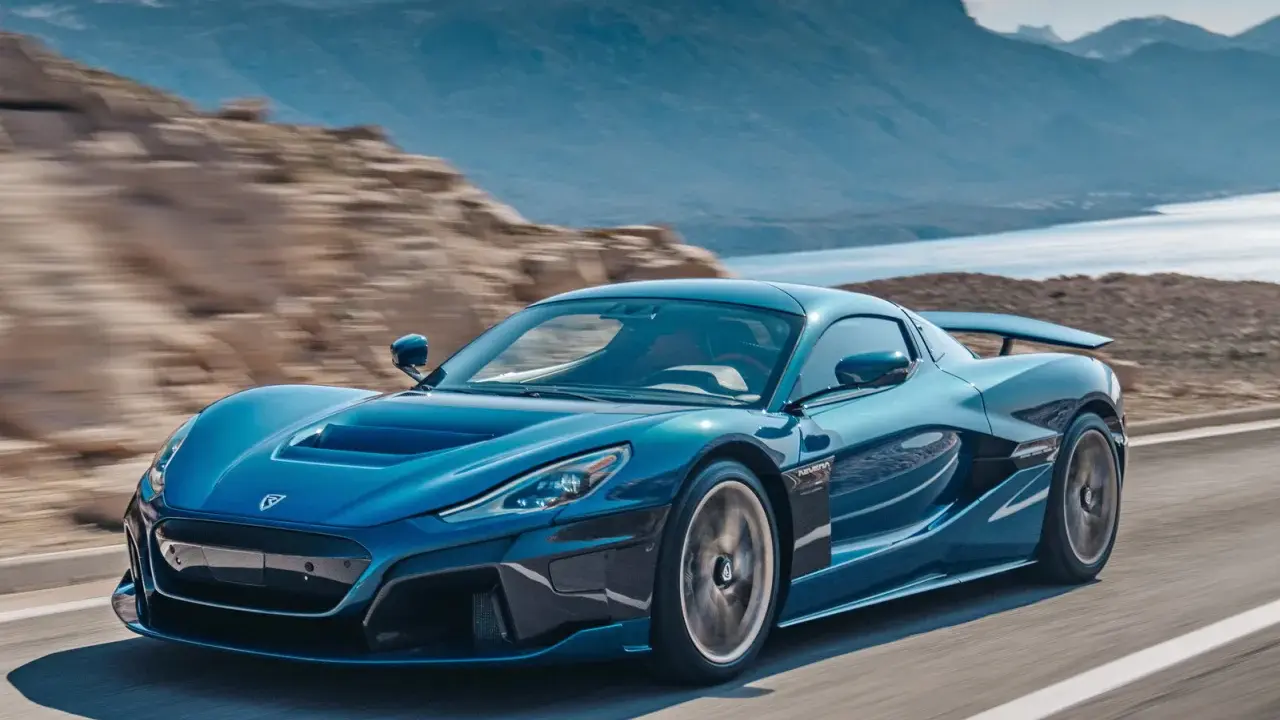 La Rimac Nevera blu sfreccia su una strada panoramica, con montagne e acqua sullo sfondo.