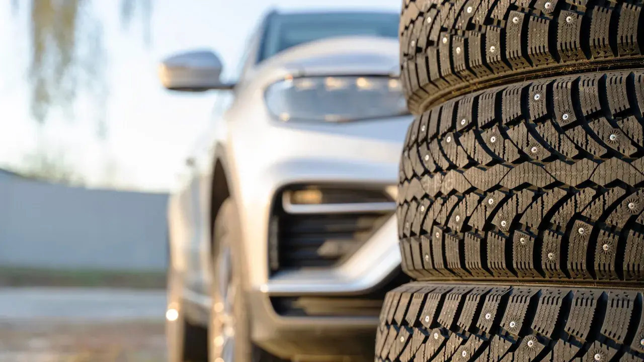 Gomme chiodate in primo piano, con un'auto bianca sfocata sullo sfondo. Mi chiedo se posso montare gomme con altezza diversa per affrontare ogni tipo di terreno.