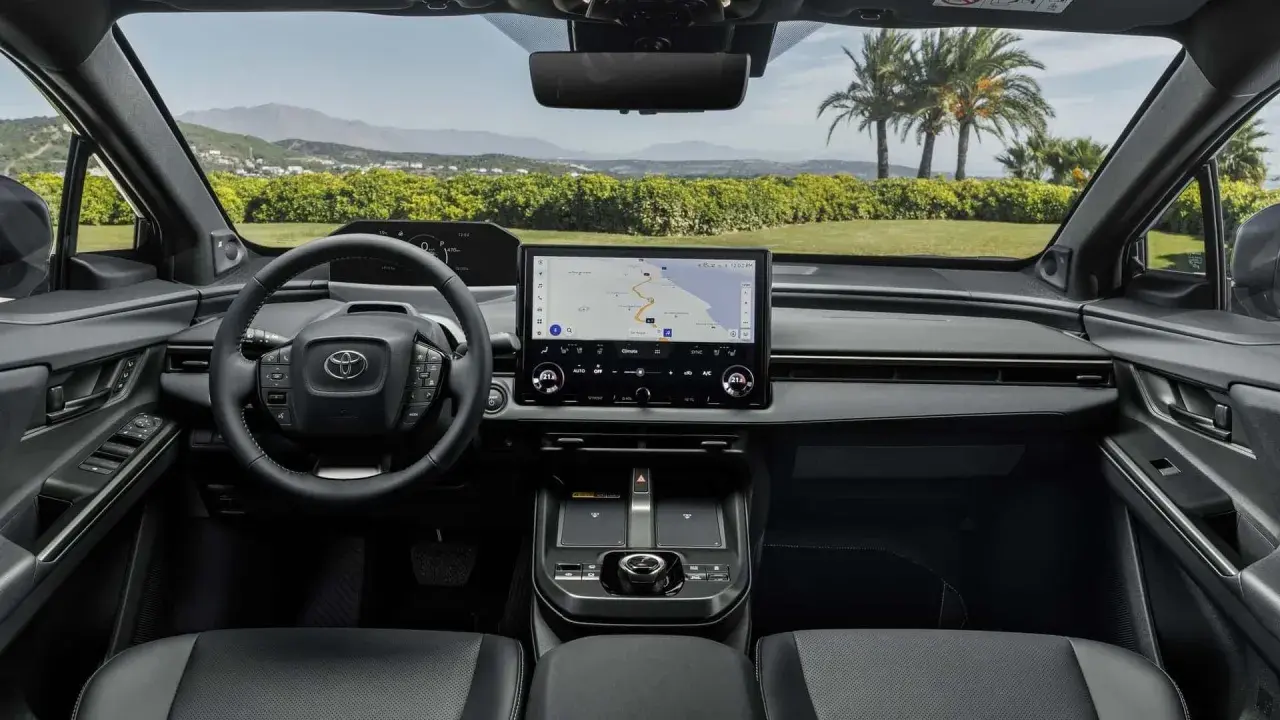 Interni moderni della Toyota bz4x con ampio display centrale e volante multifunzione. Navigazione attiva per un viaggio panoramico.