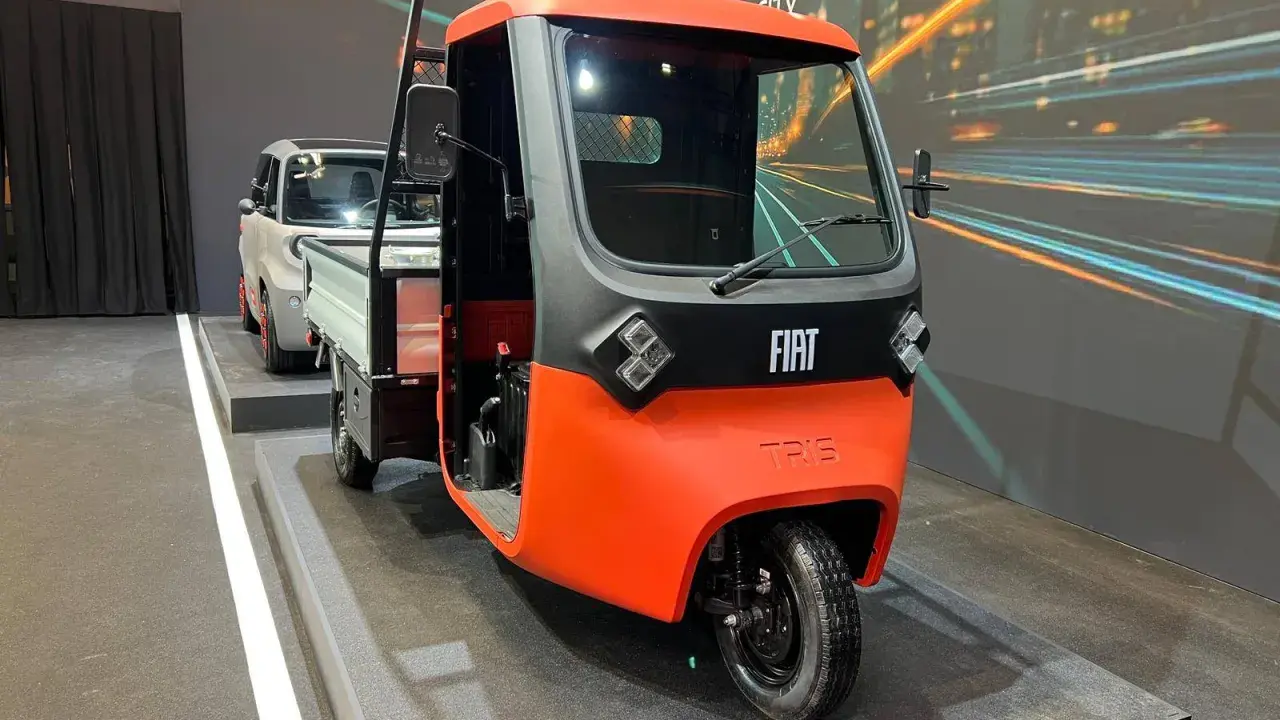Un vivace Fiat Tris arancione e grigio, un veicolo a tre ruote per il trasporto merci, esposto su una pedana.