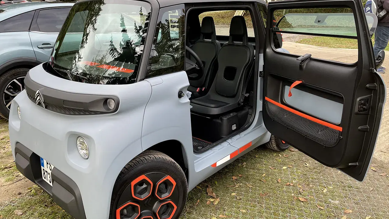 Un'auto elettrica due posti grigia con dettagli arancioni, porte aperte, sedili neri e cerchi distintivi.