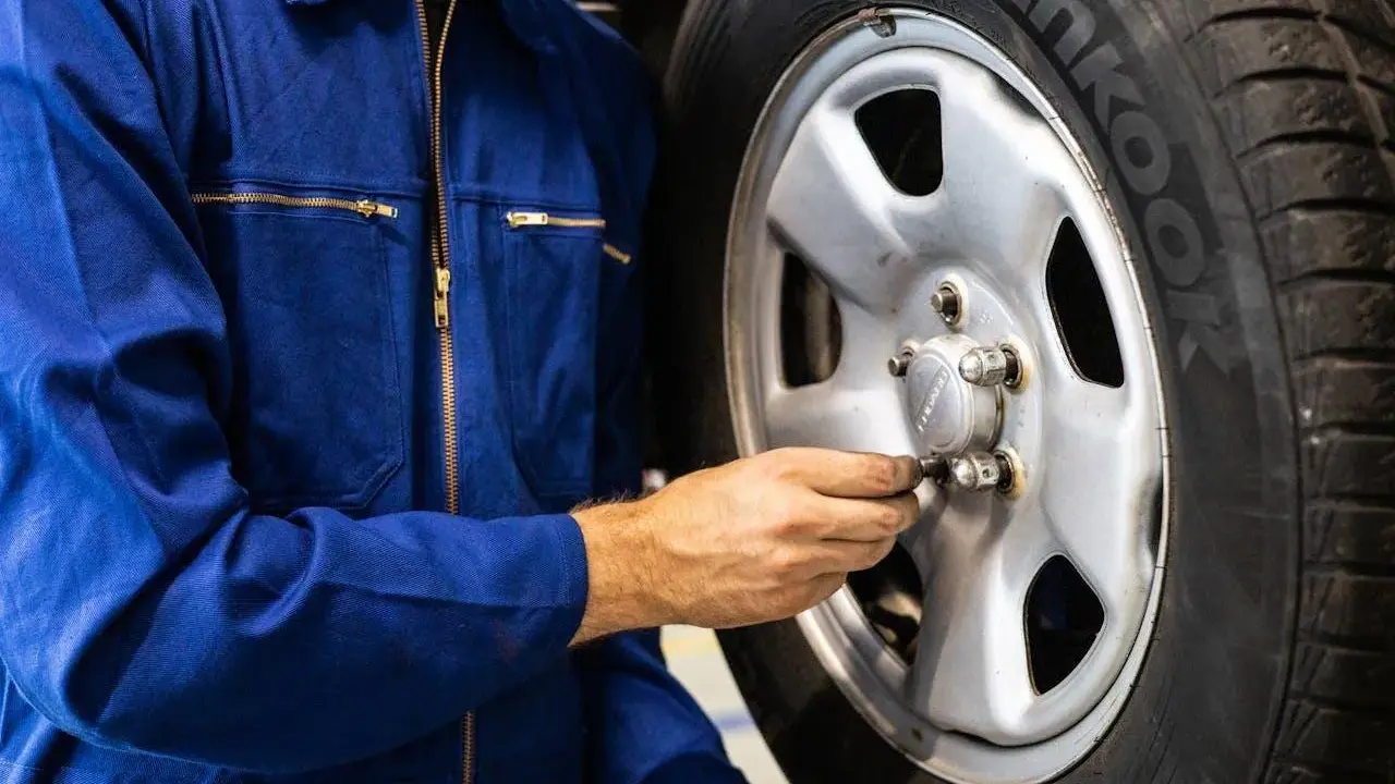 Meccanico in tuta blu controlla i bulloni di una ruota. Ci si chiede dopo quanti km si cambiano le gomme per sicurezza.