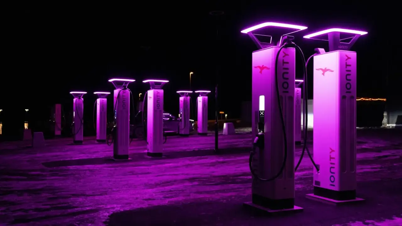 Stazione di ricarica Ionity Italia di notte, illuminata da luci viola. Colonne moderne con logo e cavi pronti per le auto elettriche.