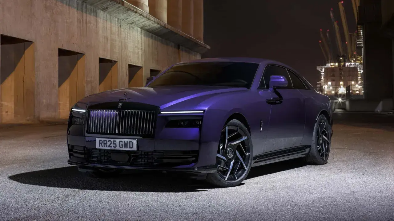 Una Rolls-Royce sportiva viola metallizzato, con un design audace e cerchi neri, parcheggiata di notte vicino a un porto industriale.