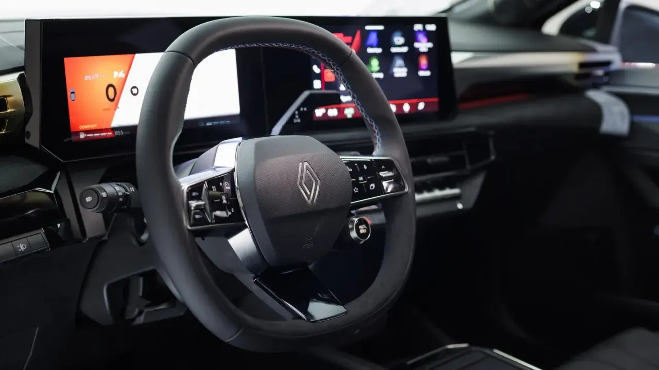Volante e cruscotto digitale con schermi moderni, dettagli blu e logo Renault. Interni della nuova Clio 2026.