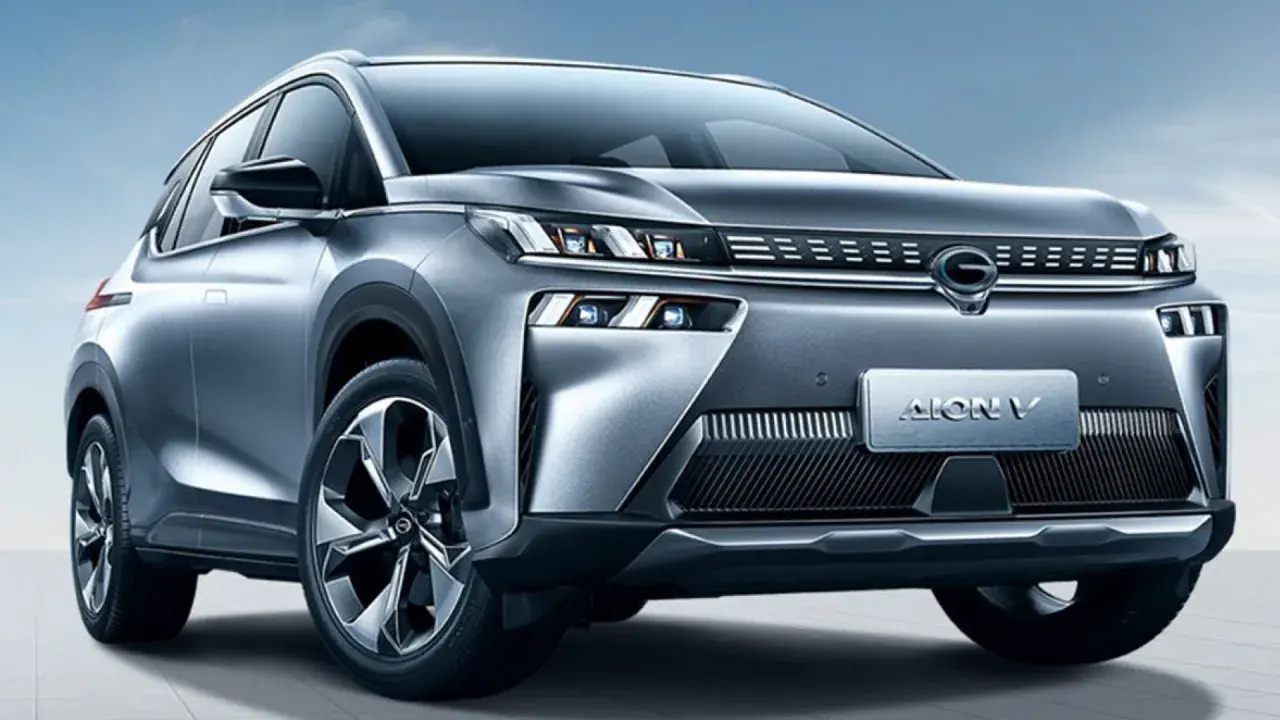 Un SUV grigio metallizzato, l'Aion V, con un design moderno e fari a LED affilati, si presenta su uno sfondo blu cielo.