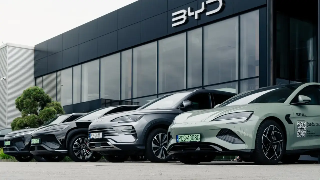 Vari modelli di auto BYD parcheggiati davanti a uno showroom moderno.
