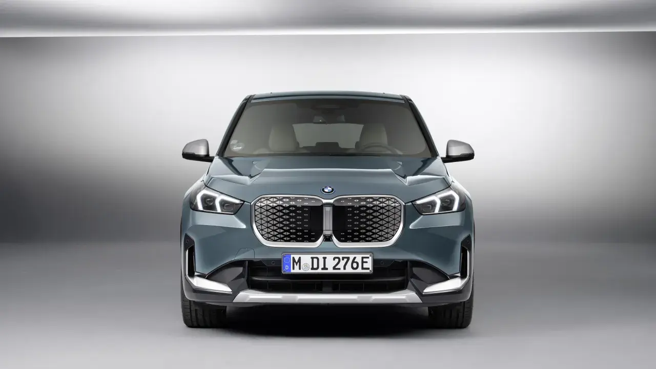 La BMW iX1, con la sua impressionante autonomia, si presenta frontalmente in un ambiente minimalista.