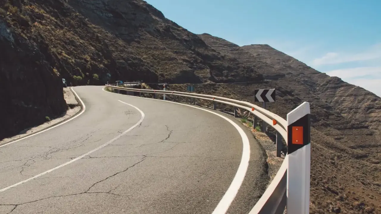 Strada tortuosa in montagna con guardrail e segnali di pericolo. I catadiottri cosa sono? Sono quei dispositivi che riflettono la luce per segnalare la strada.