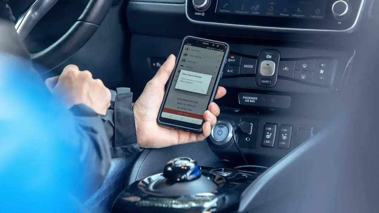 Mano che tiene uno smartphone con app di navigazione attiva, mostrando il **power cruise control** per un viaggio in auto.
