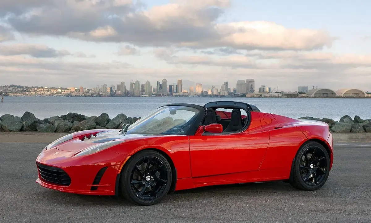 Tesla Roadster rosso fiammante, con la silhouette di una città all'orizzonte.