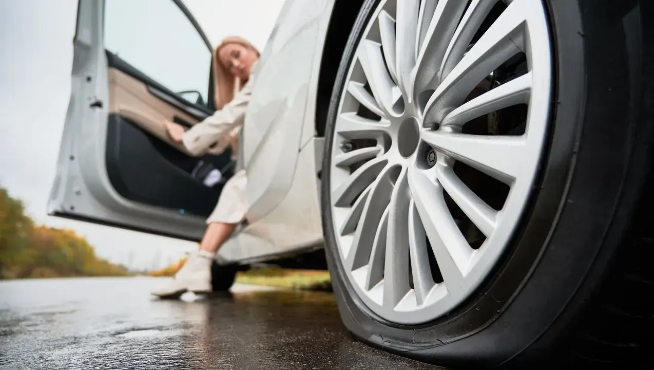 Donna esce dall'auto con gomme sgonfie sul bagnato.
