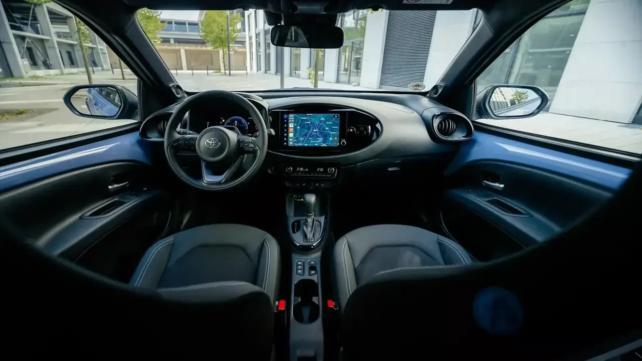 Interni moderni della Toyota Aygo X: volante, cruscotto con navigatore e sedili in tessuto.