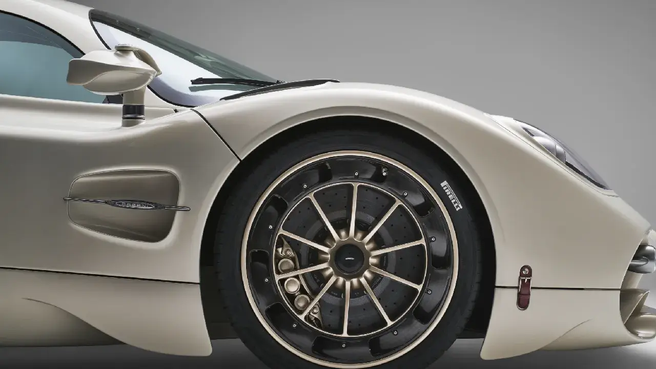 Dettaglio di un'auto sportiva color champagne, con focus sul montaggio pneumatici e cerchi in lega dorati.