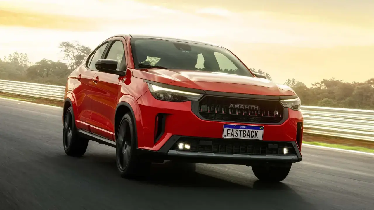 La Fiat Fastback 2026 rossa sfreccia su una pista, con il sole che illumina il cielo.