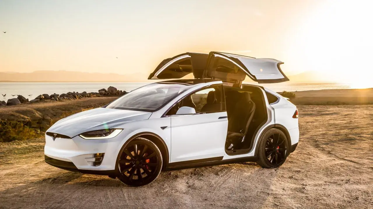 Tesla Model X bianca con portiere ad ali di gabbiano aperte al tramonto, un'auto elettrica che rappresenta il lusso e l'innovazione, forse la tesla più costosa.