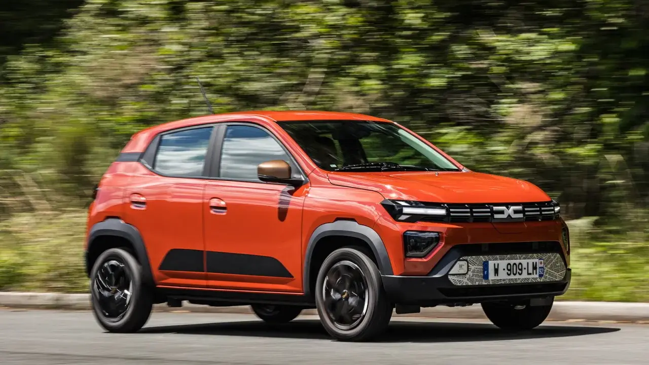 Dacia Spring arancione in movimento, la sua compatta lunghezza la rende ideale per la città.