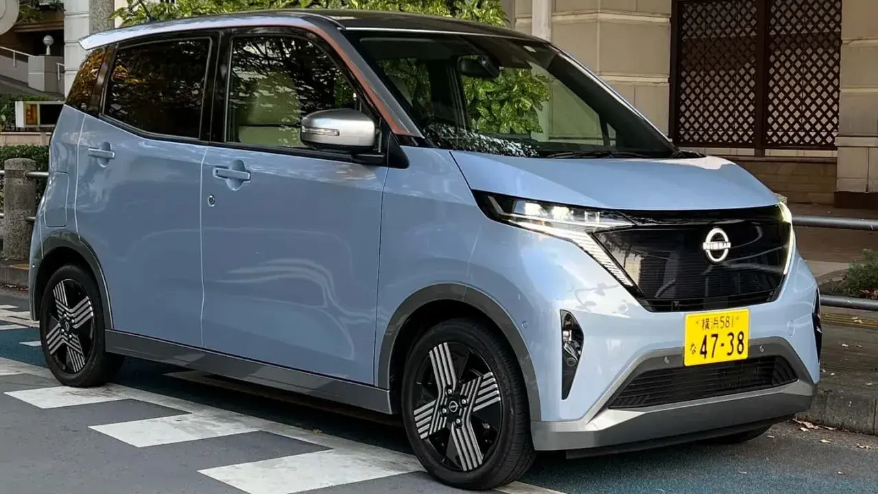 Nissan Sakura azzurro pastello, un'auto elettrica compatta con dettagli color rame sul tetto, parcheggiata su strisce pedonali.