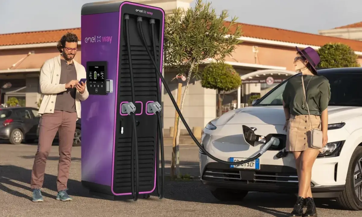 Coppia in una stazione di ricarica Enel X Way. Lei attende mentre l'auto si carica, lui controlla lo smartphone. Ottime recensioni per questa stazione di ricarica.
