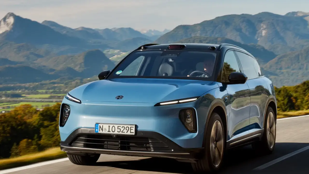 NIO ES6 blu sfreccia su una strada panoramica tra montagne verdi.