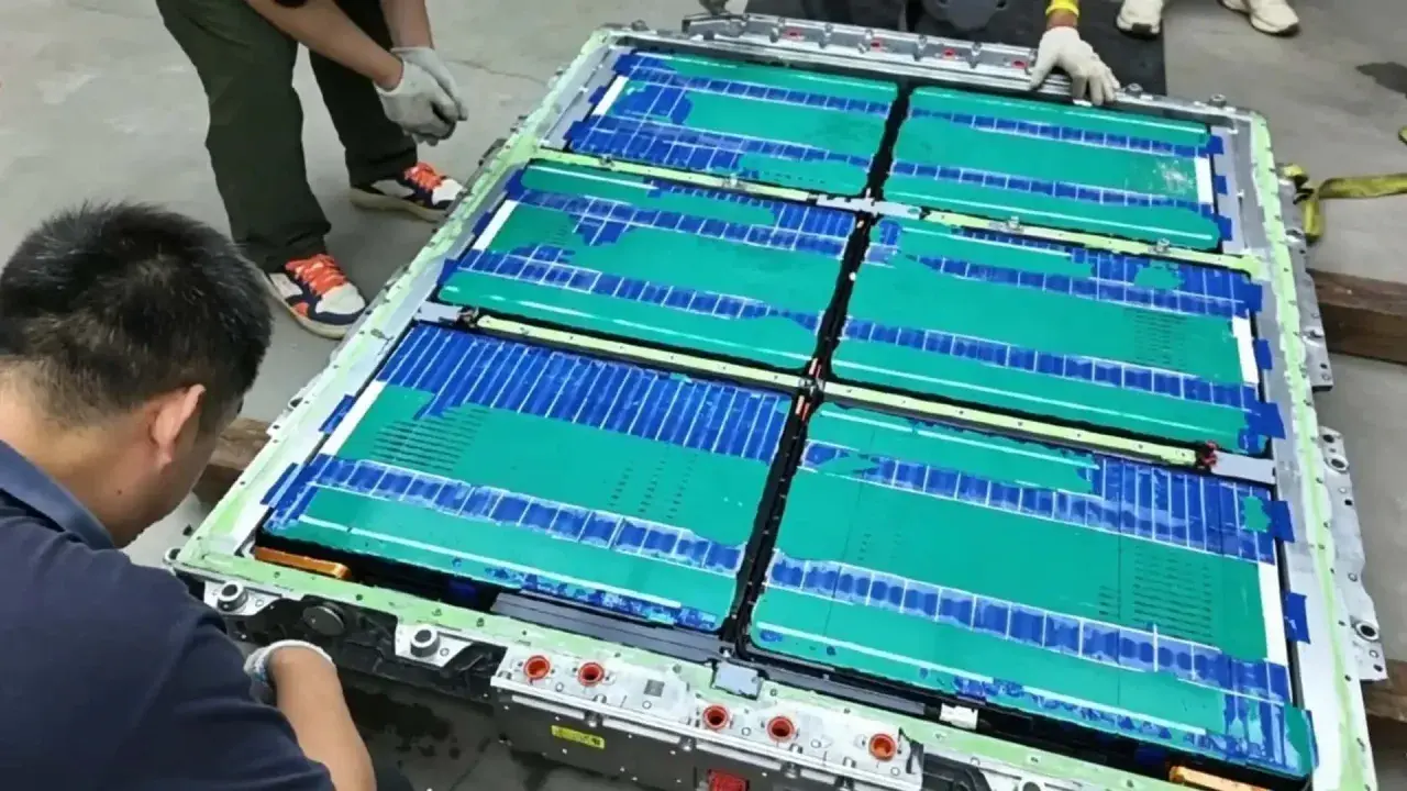 Un tecnico lavora su un pacco batteria, con celle verdi e blu che ricordano una blade battery.