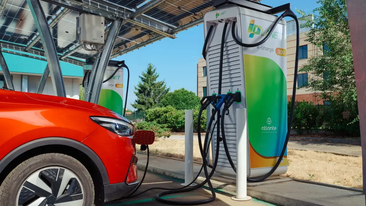 Un'auto rossa si ricarica presso colonnine ultra fast sotto pannelli solari.