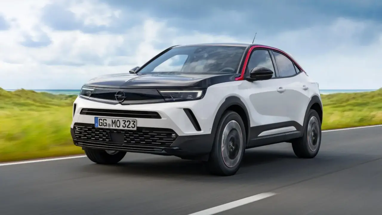 Opel Mokka bianco e nero con tetto rosso, su strada panoramica. Nonostante il design accattivante, alcuni utenti segnalano opel mokka difetti.