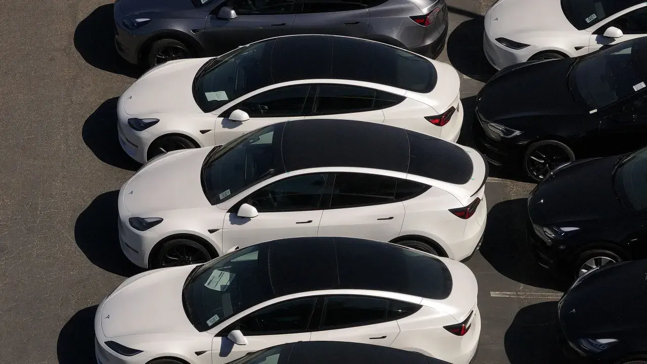 Parcheggio di auto elettriche in Italia, con modelli bianchi e grigi in fila, pronti per la consegna.