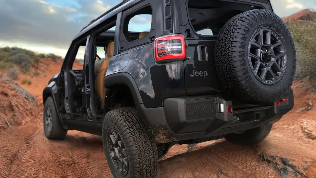 Un fuoristrada elettrico Jeep nero affronta un sentiero sterrato nel deserto, con le portiere aperte e una ruota di scorta sul retro.