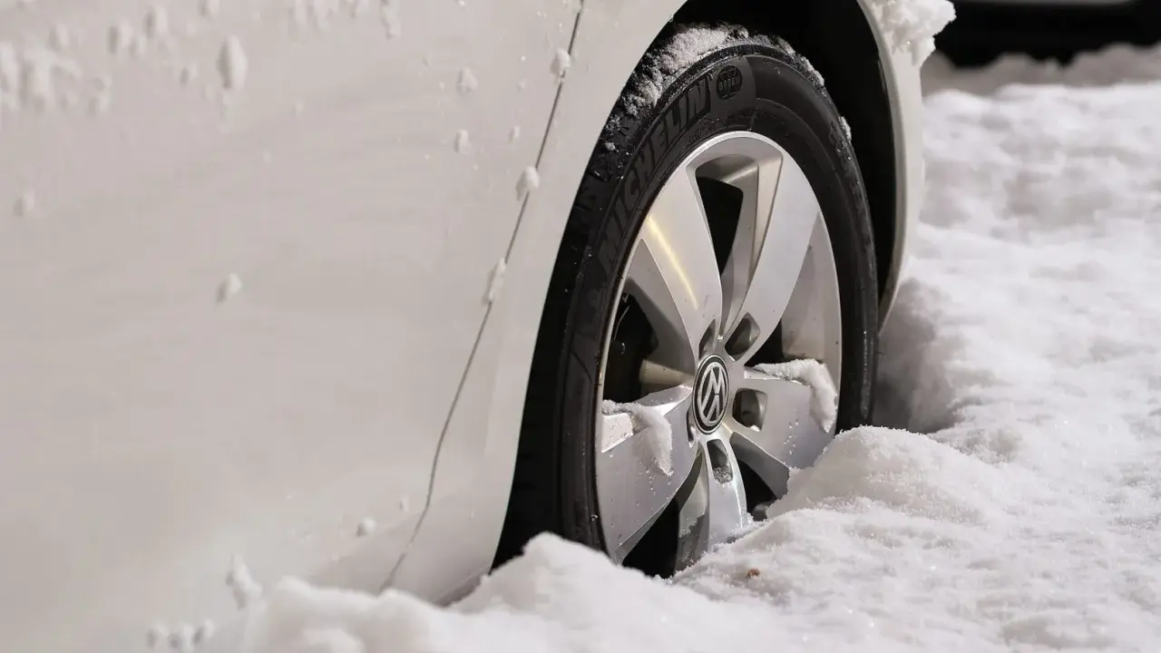 Ruota di un'auto bianca sommersa dalla neve. Il freno a mano ghiacciato rende difficile muoversi.