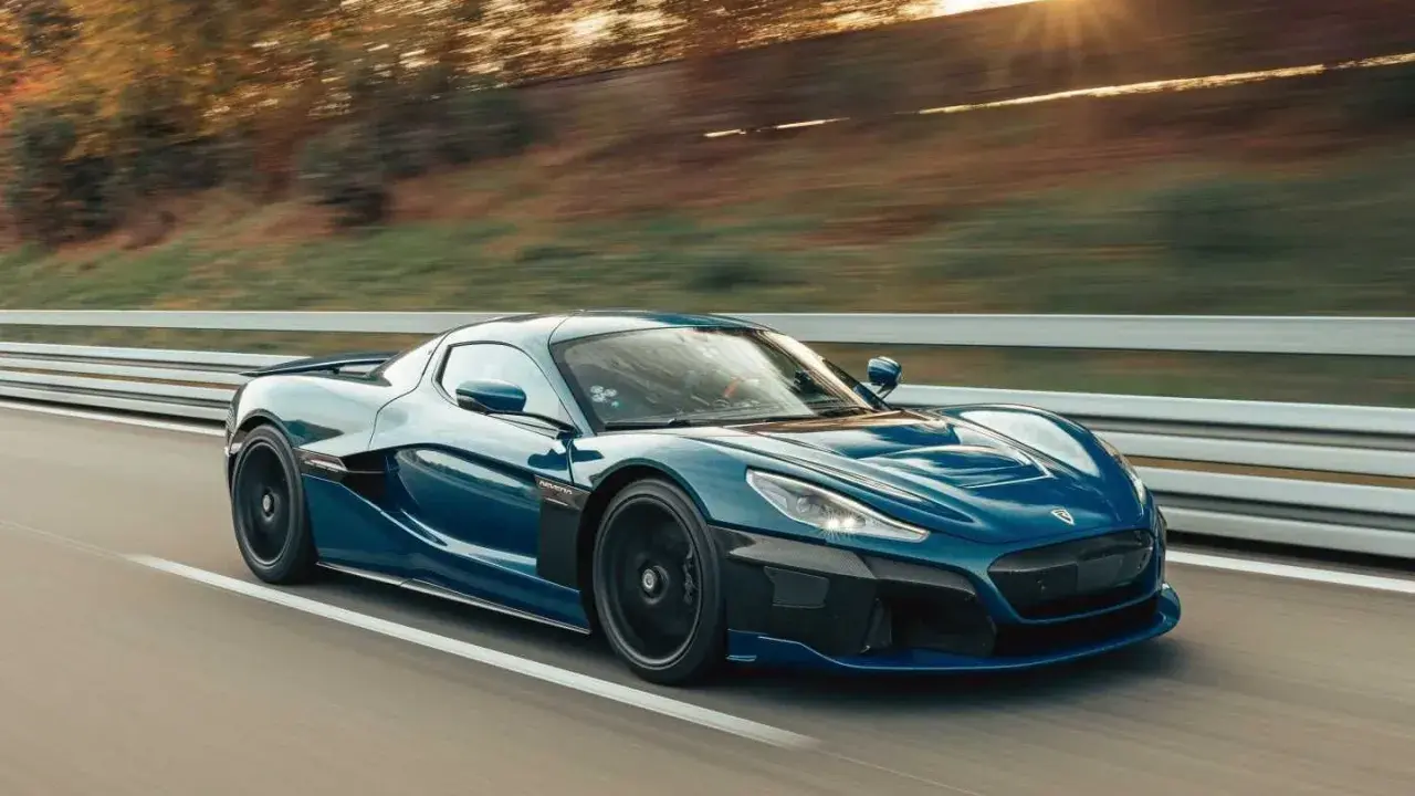 La **auto elettrica più veloce** sfreccia su una strada, con il sole che tramonta tra gli alberi sullo sfondo.