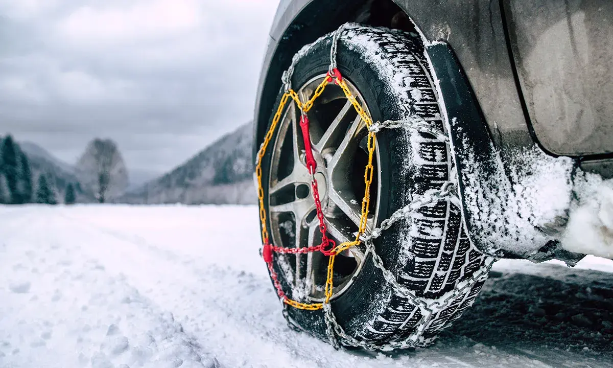 Catene da neve senza codice: come riconoscerle. Ruota di un'auto con catene montate su strada innevata.