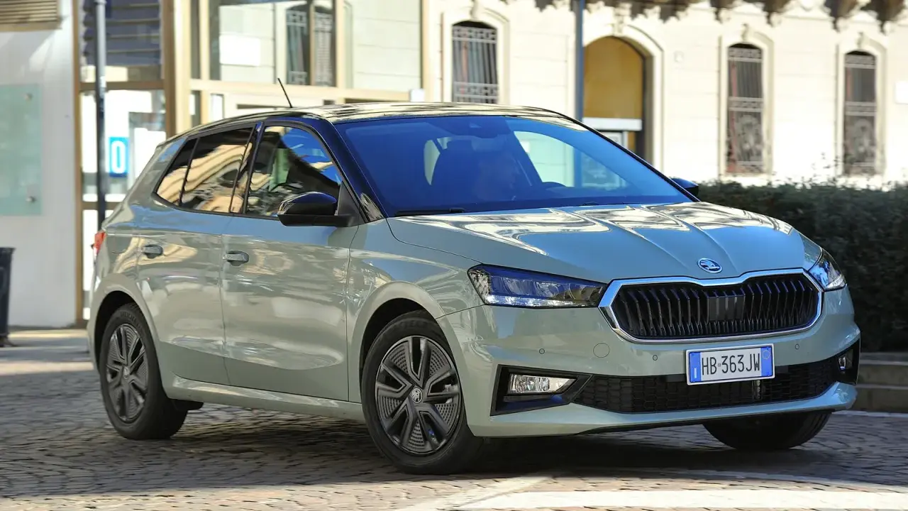 A light green Skoda Fabia hatchback with a black roof is parked on a cobblestone street in front of a building.