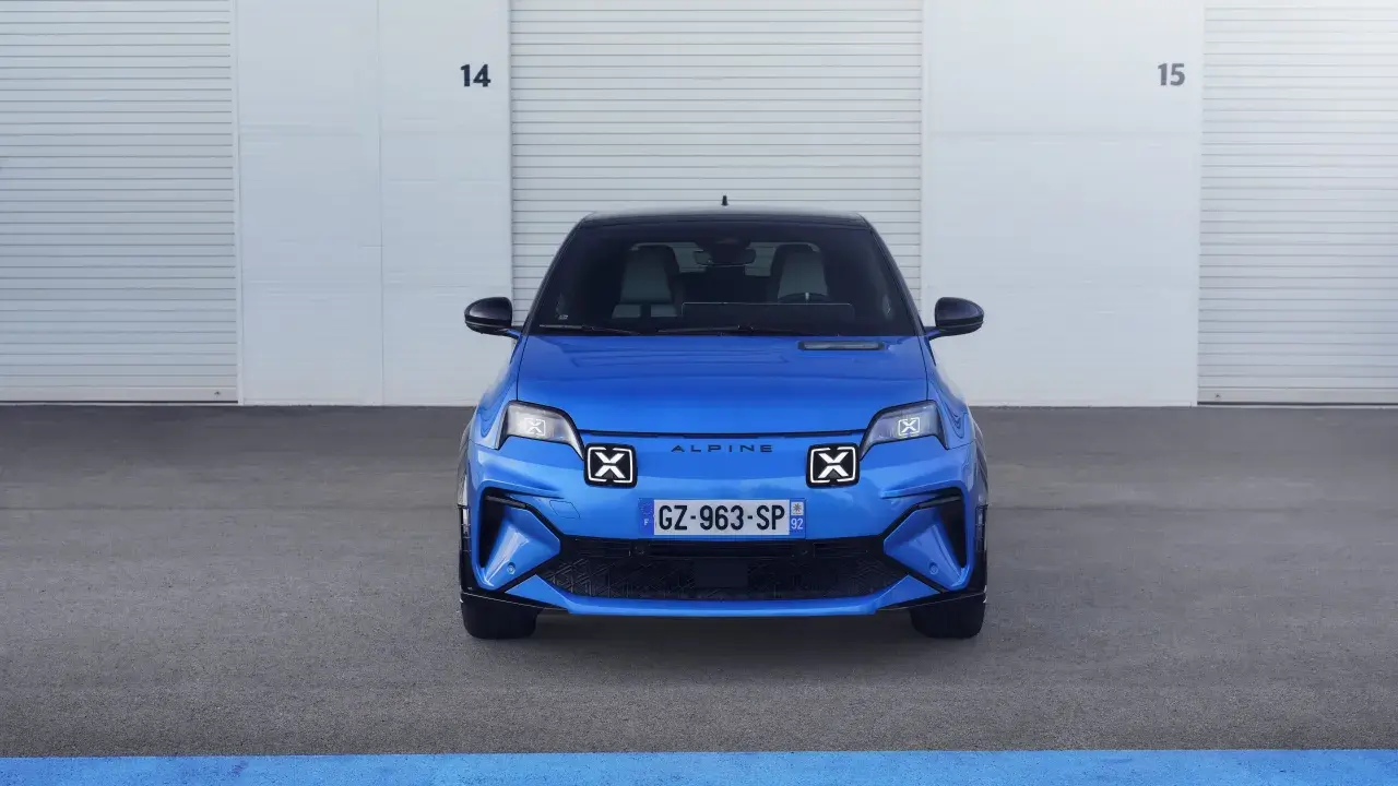 La nuova Alpine A290, un'auto elettrica sportiva blu brillante, attende il suo momento davanti a un garage con porte chiuse.