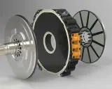 Componenti di un motore a flusso assiale: albero, statore nero con anello bianco e rotore a disco con magneti.