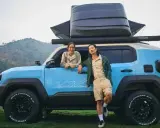 Coppia sorridente accanto a un toyota land cruiser mini blu, pronto per l'avventura con tettoia e box sul tetto.